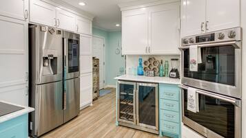 A kitchen with stainless steel appliances, white cabinets, a blue countertop, and a built-in wine cooler.