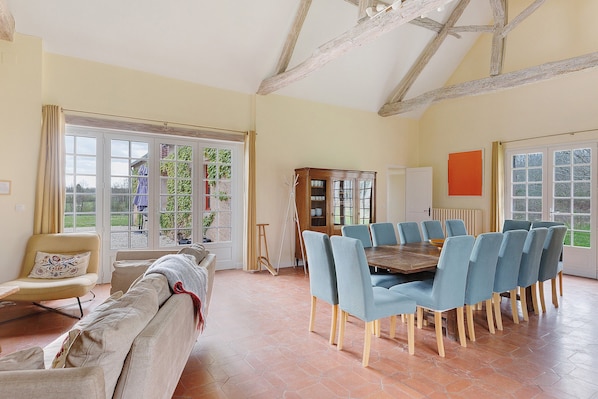 A dining area with a wooden table and blue chairs, a sofa, and a view through large windows.