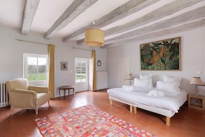 A bedroom with a bed, a chair, a radiator, a window, and a painting on the wall.