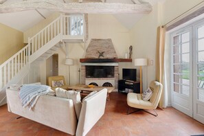 Ein Wohnzimmer mit Kamin, einer Couch, einem Sessel, einem Fernseher und einer Treppe.