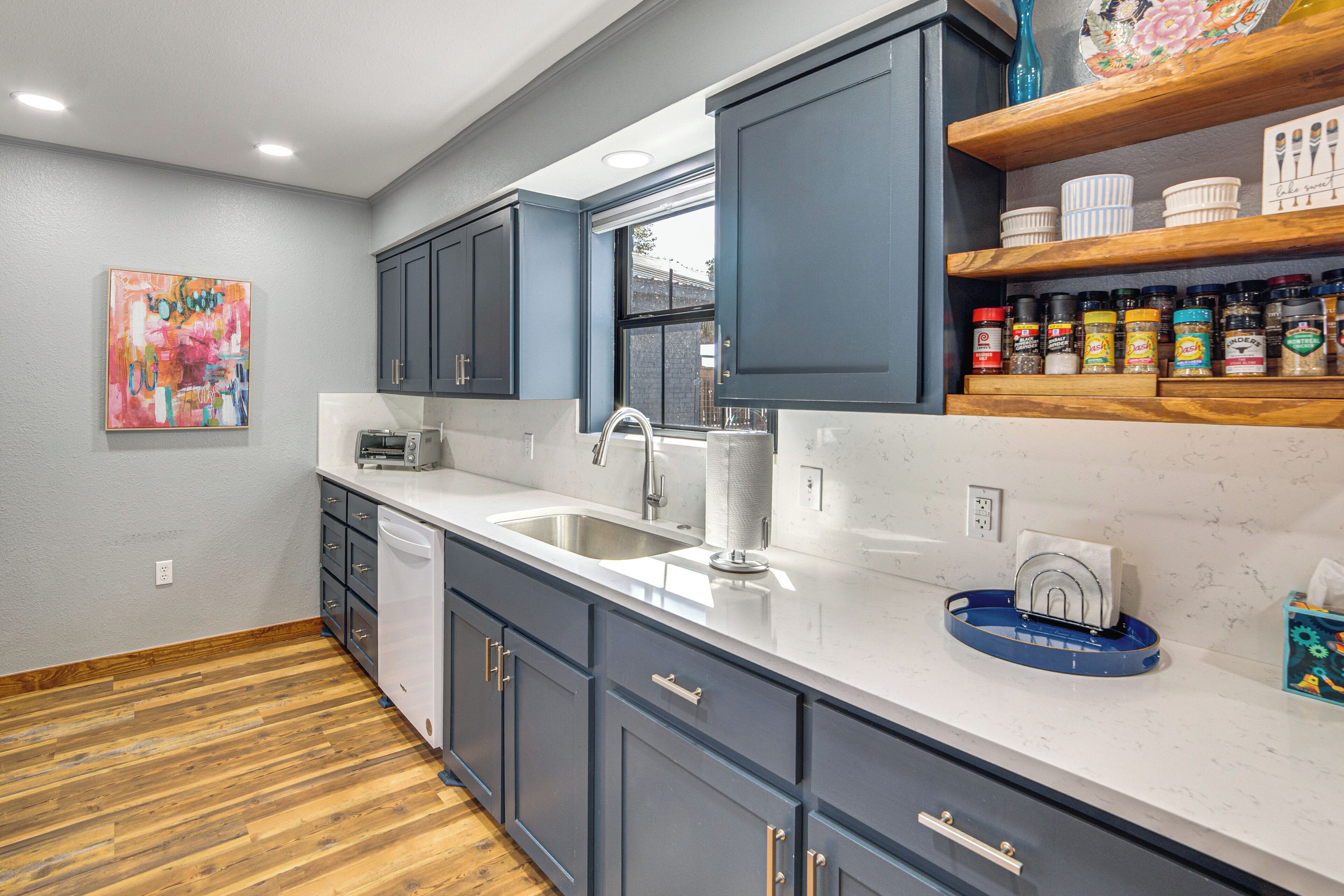 A modern kitchen with grey cabinets, a white countertop, and a wooden floor.