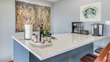 A kitchen with a central island, a coffee machine, and a large tapestry on the wall.