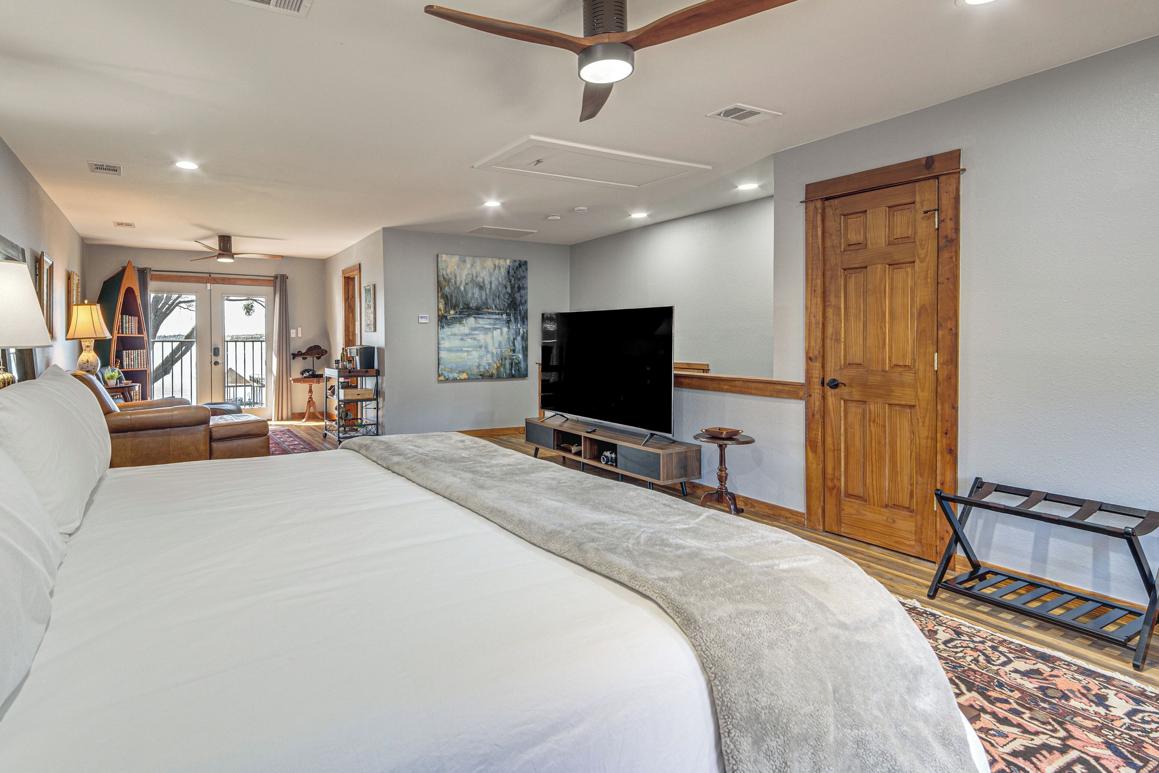 A spacious bedroom with a large bed, a television, a wooden door, and a view through a glass door.