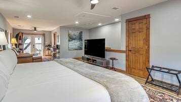 A spacious bedroom with a large bed, a television, a wooden door, and a view through a glass door.