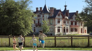 Una piscina con valla de madera, un edificio grande con varias chimeneas y una torre al fondo.