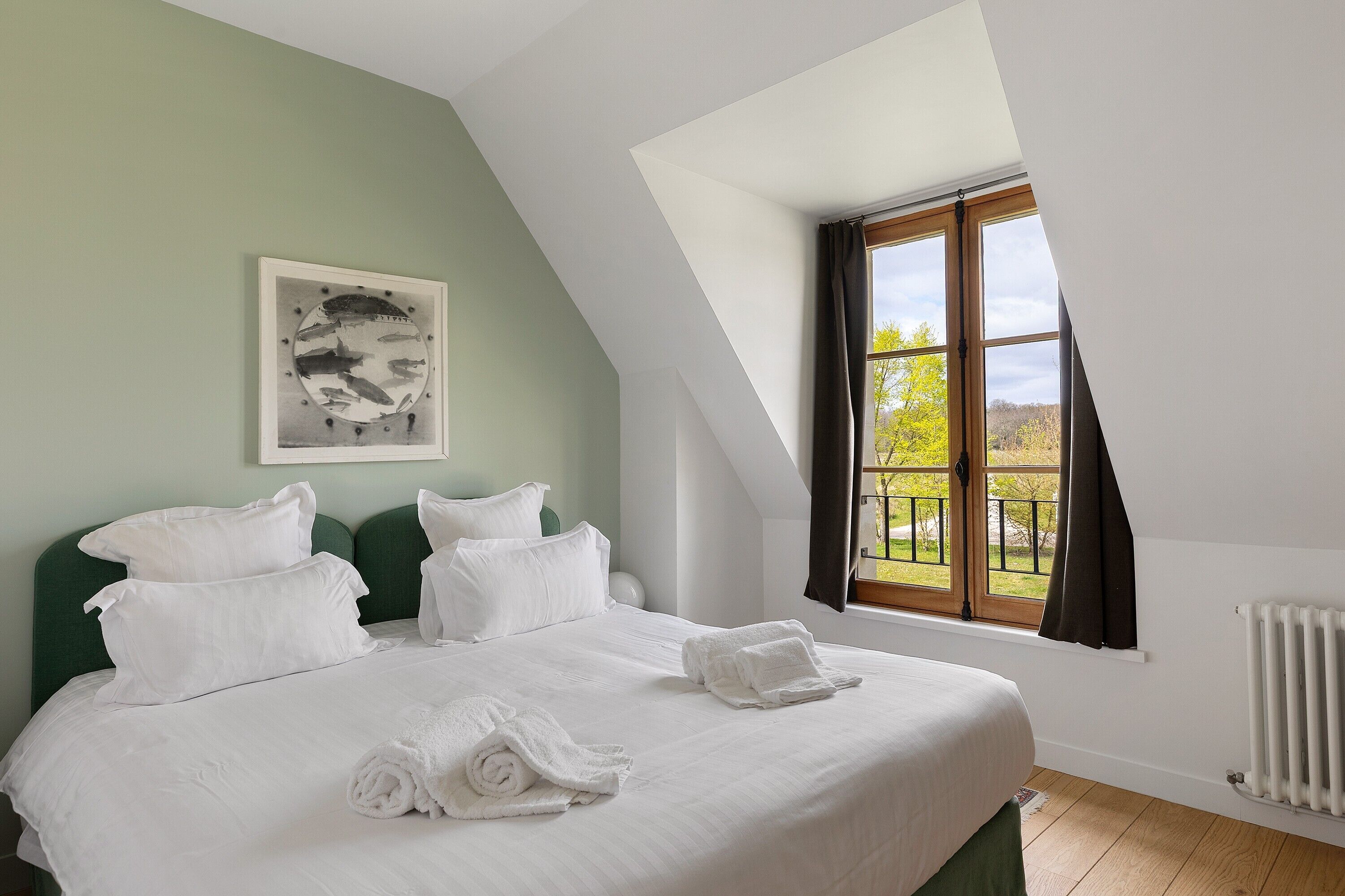 A bedroom with a large bed, a window with curtains, a radiator, and a painting on the wall.
