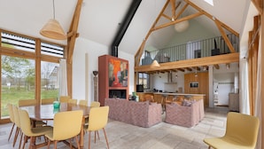 Un comedor amplio con una gran mesa de madera y sillas amarillas, un rincón de descanso acogedor con cojines estampados, y una cocina al fondo.