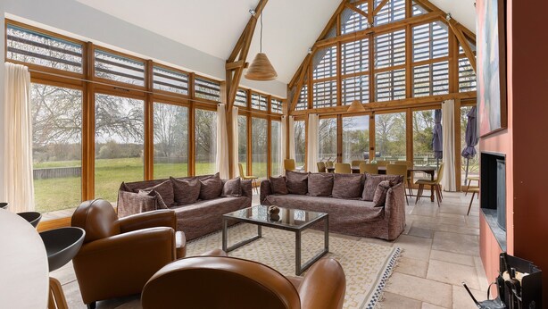 Amplia sala de estar con ventanas grandes, chimenea y techo alto con vigas de madera.