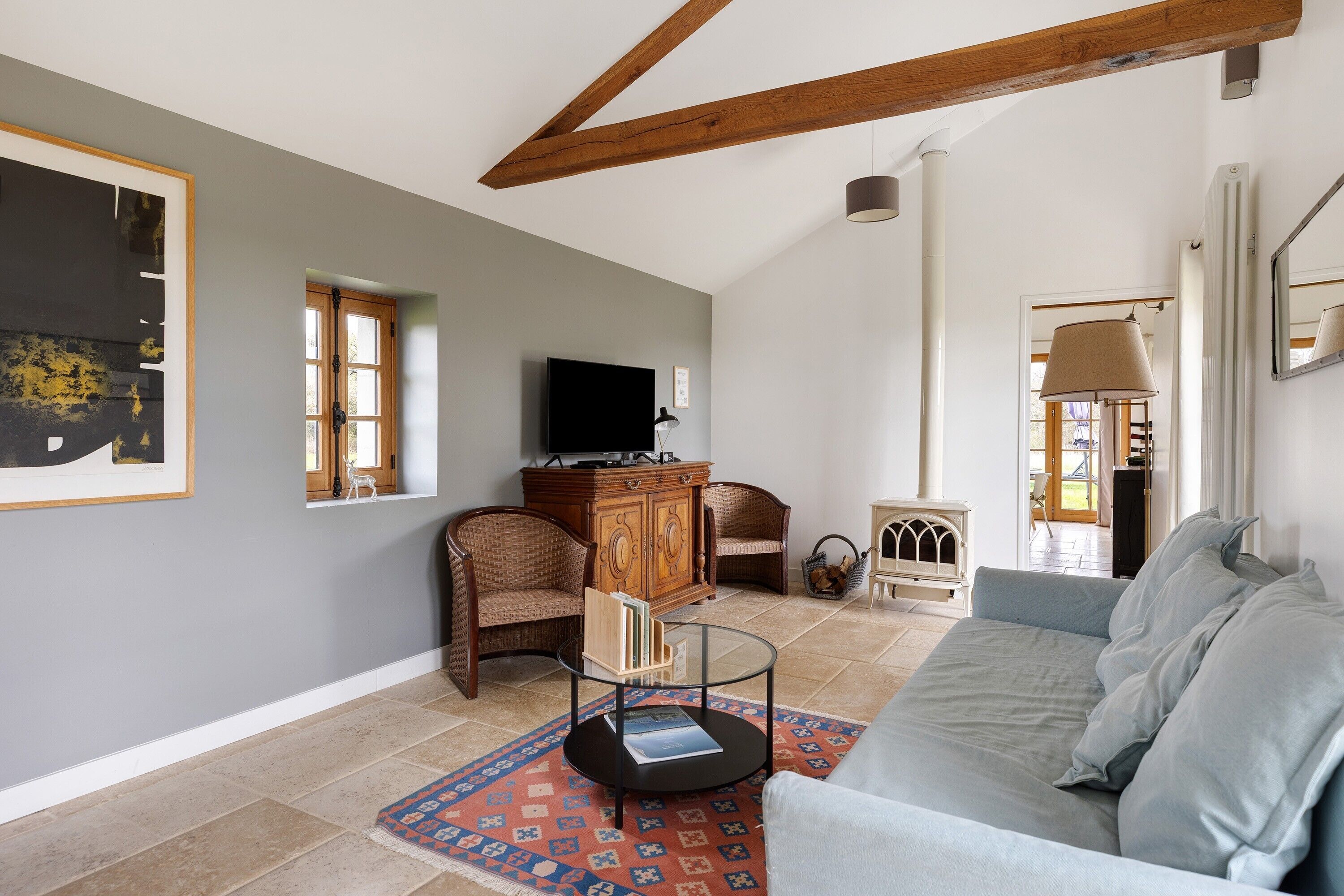 Un salon comprenant un canapé, une table basse en verre, des fauteuils en osier, un meuble en bois et un téléviseur.