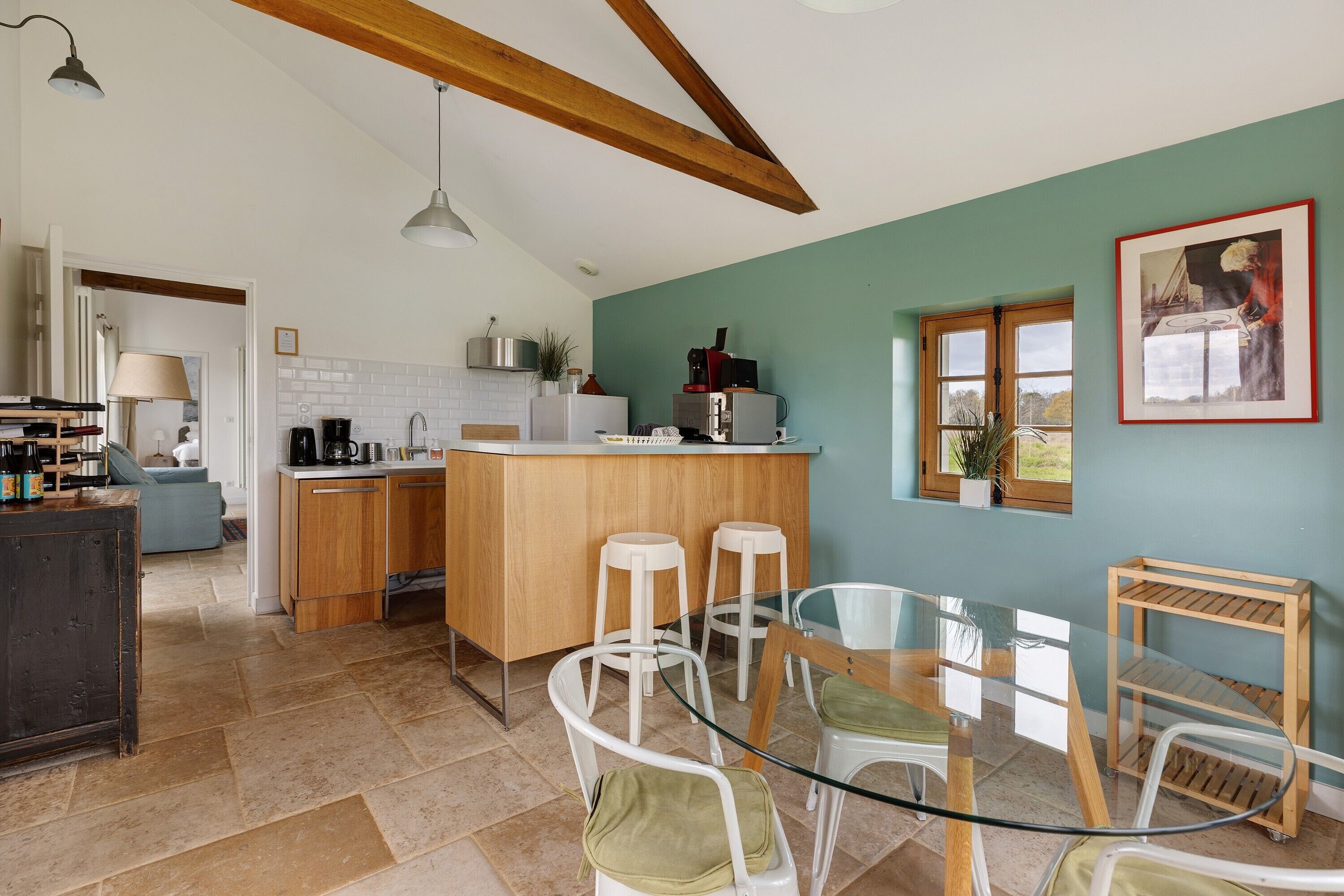 A kitchen with a bar area, white bar stools, a glass dining table, and a wooden ceiling.