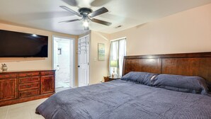 Une chambre à coucher comprenant un lit, une tête de lit en bois, un ventilateur de plafond, une télévision et une commode.