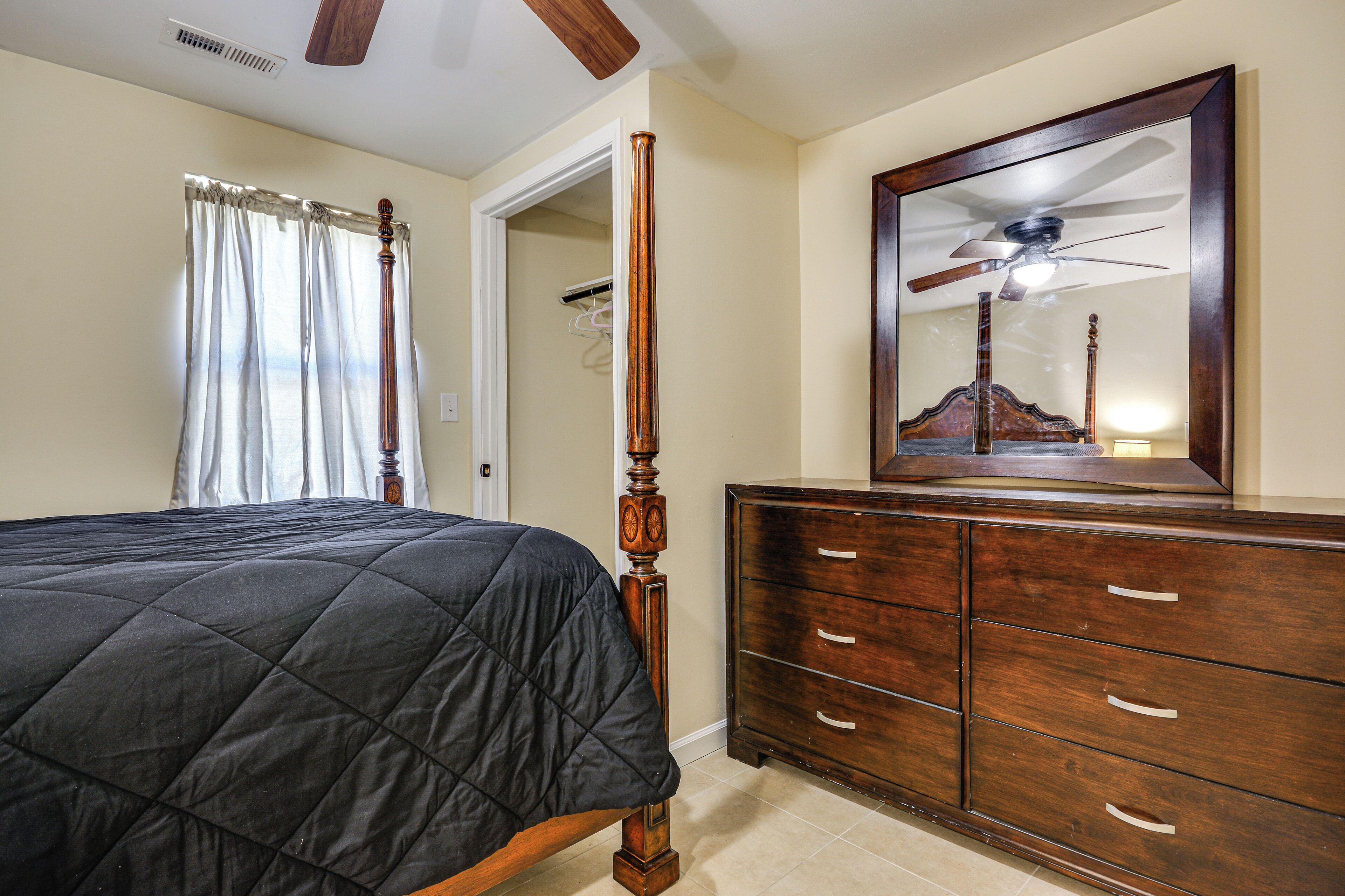 A bedroom with a bed, a wooden dresser, a mirror, and a ceiling fan.