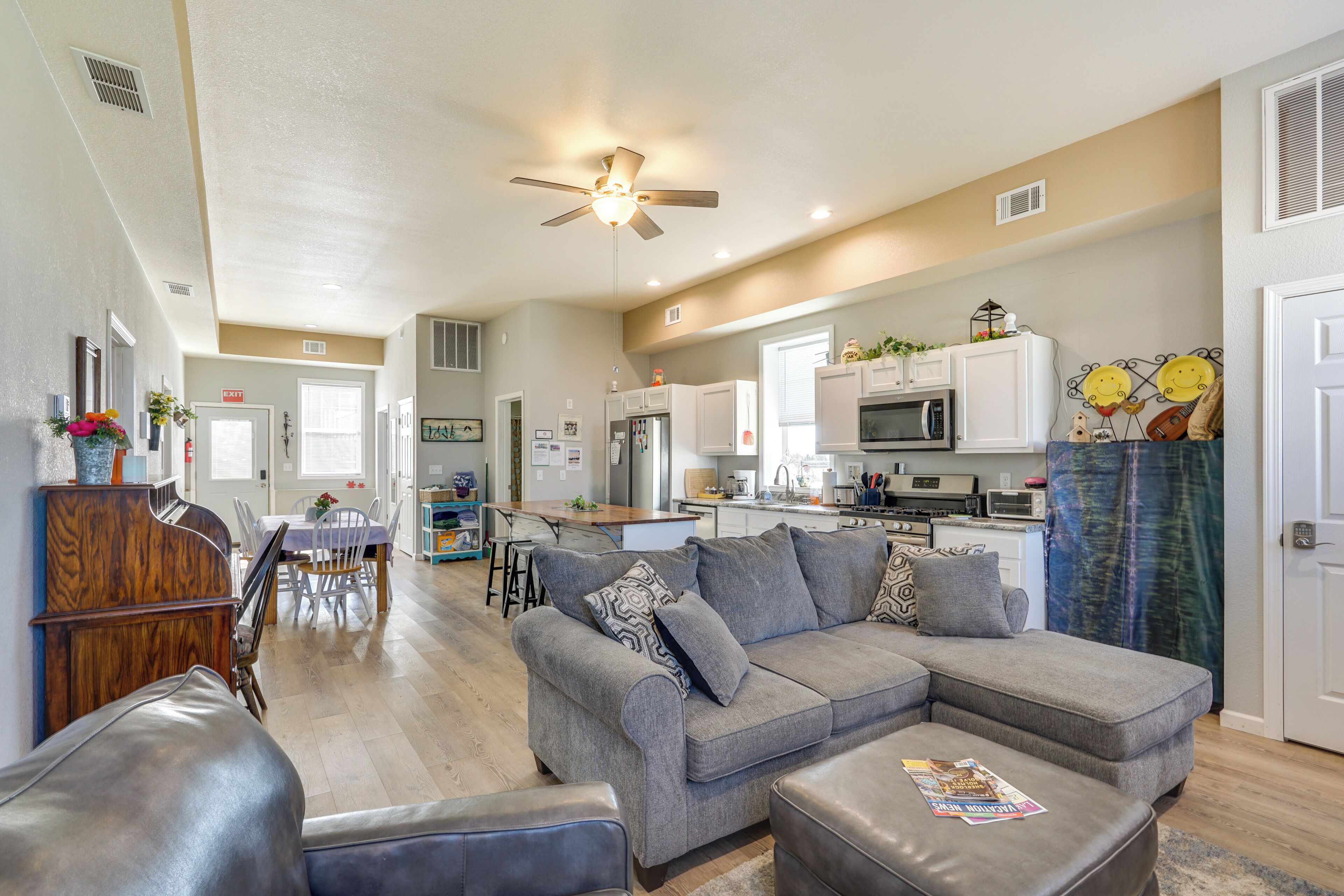 A spacious living area with a gray sectional sofa, a dining table, and a kitchen in the background.