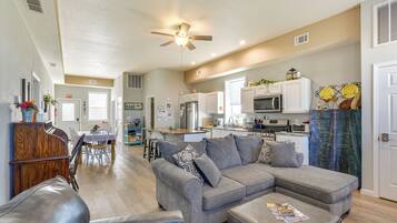 A spacious living area with a gray sectional sofa, a dining table, and a kitchen in the background.