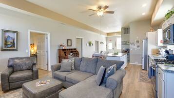 A modern kitchen with a microwave, stove, and sink, a gray sectional sofa, a leather armchair, and a ceiling fan.