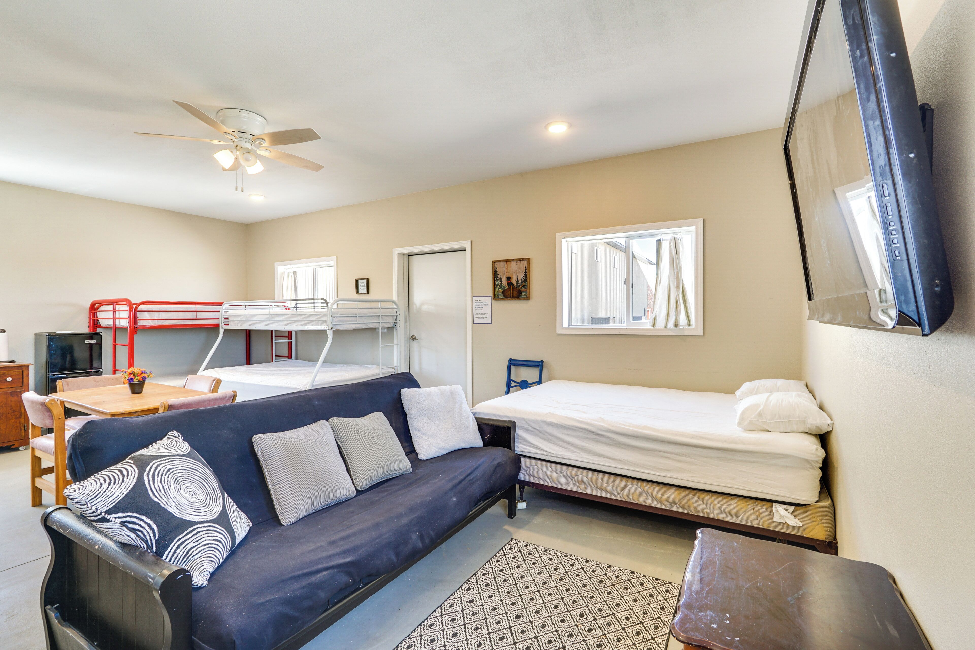 A compact room with a sofa, a single bed, a small table, a ceiling fan, and a window.