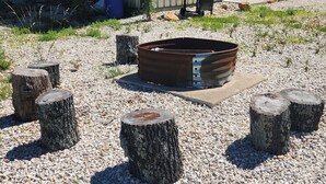 A metal fire pit surrounded by wooden stumps and gravel. - Hike & Fish! Ozarks Studio on Multi-unit Farm (Richland)