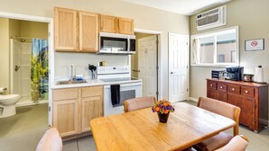 A compact kitchen with wooden cabinets, a white stove, and a dining table with chairs. - Hike & Fish! Ozarks Studio on Multi-unit Farm (Richland)