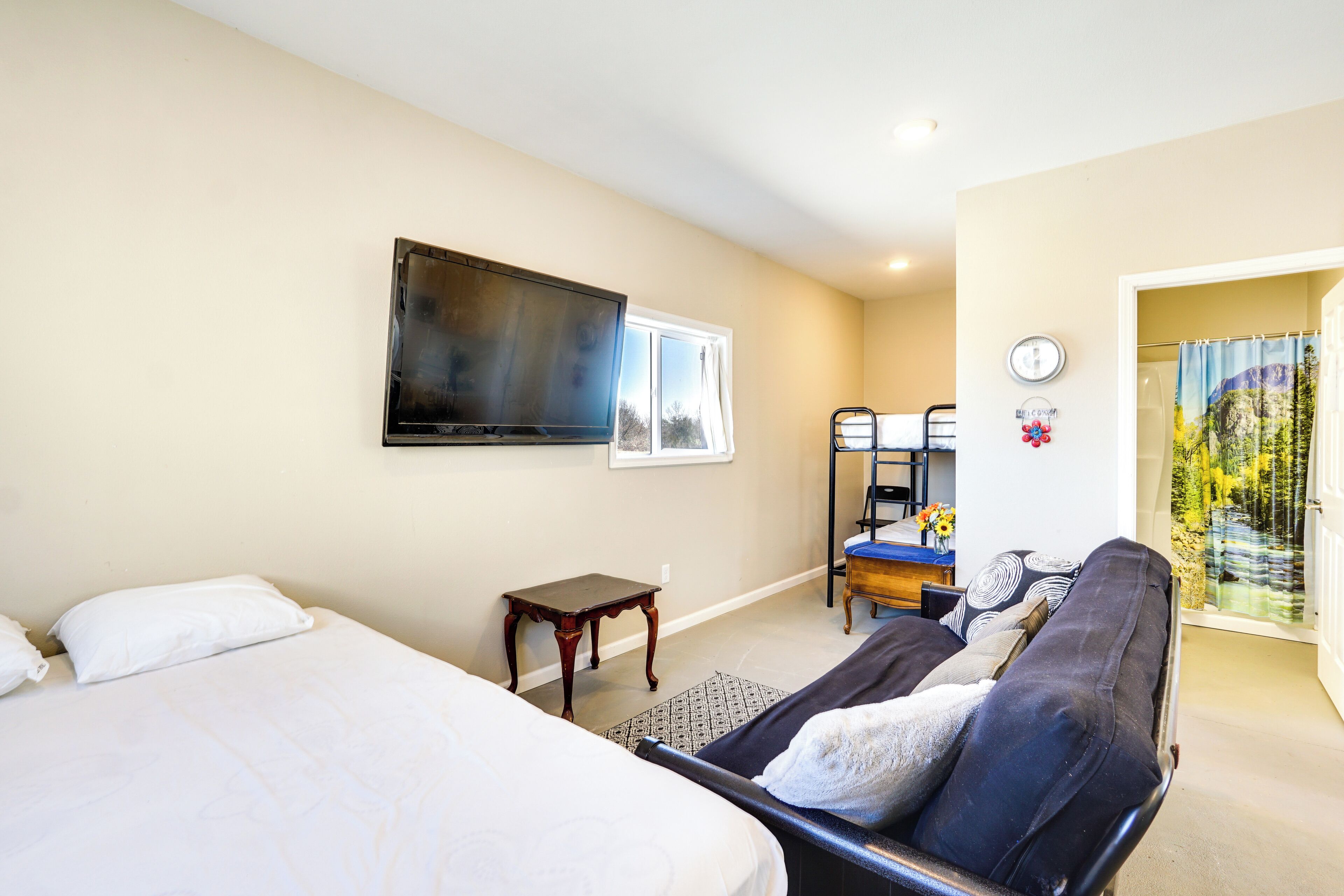 A bedroom with a bed, a sofa, a television, a small table, and a window.