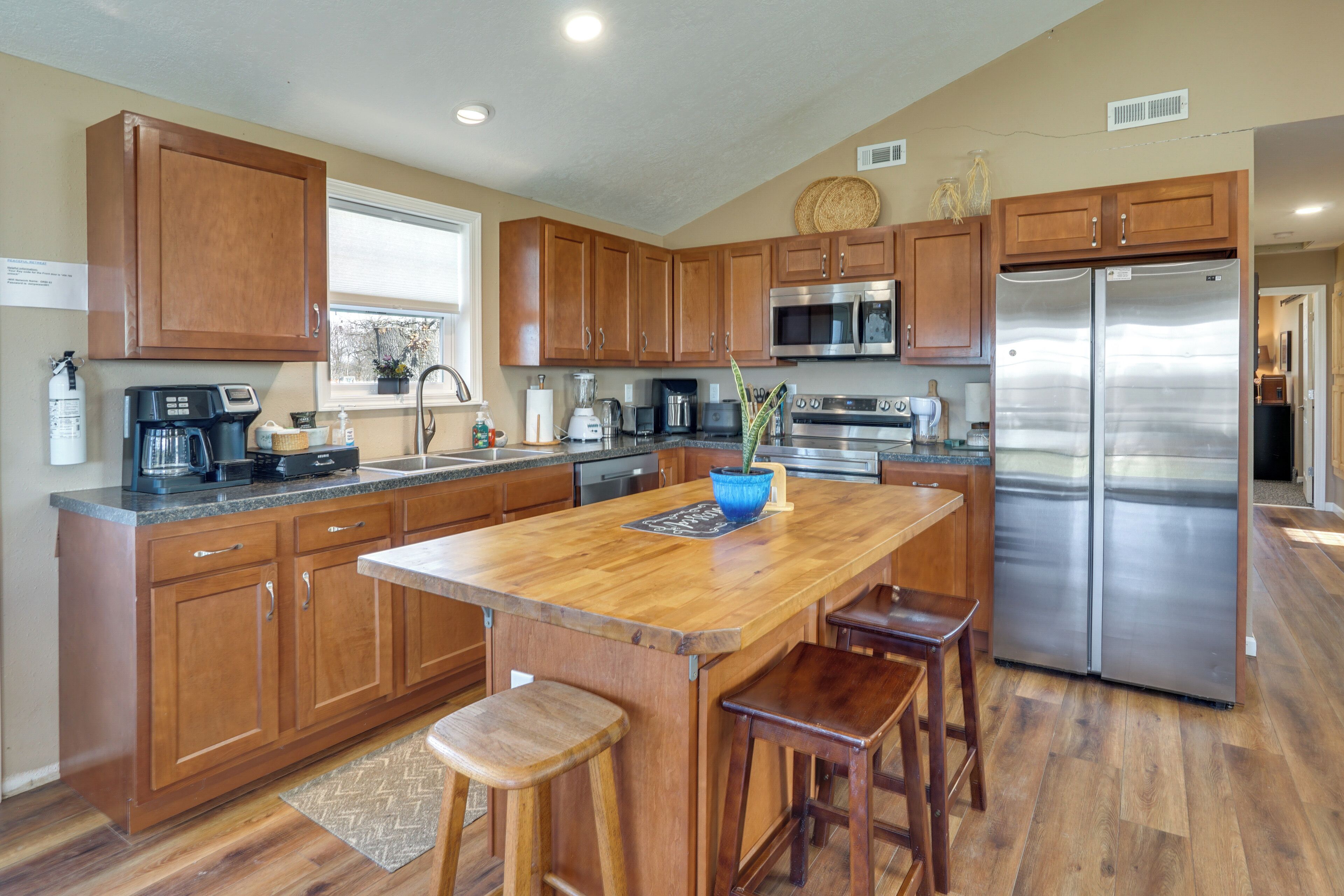 A kitchen with wooden cabinets, a stainless steel refrigerator, a coffee maker, and a large island with stools.