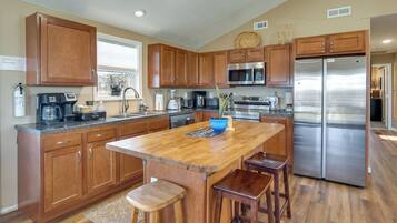 A kitchen with wooden cabinets, a stainless steel refrigerator, a coffee maker, and a large island with stools.