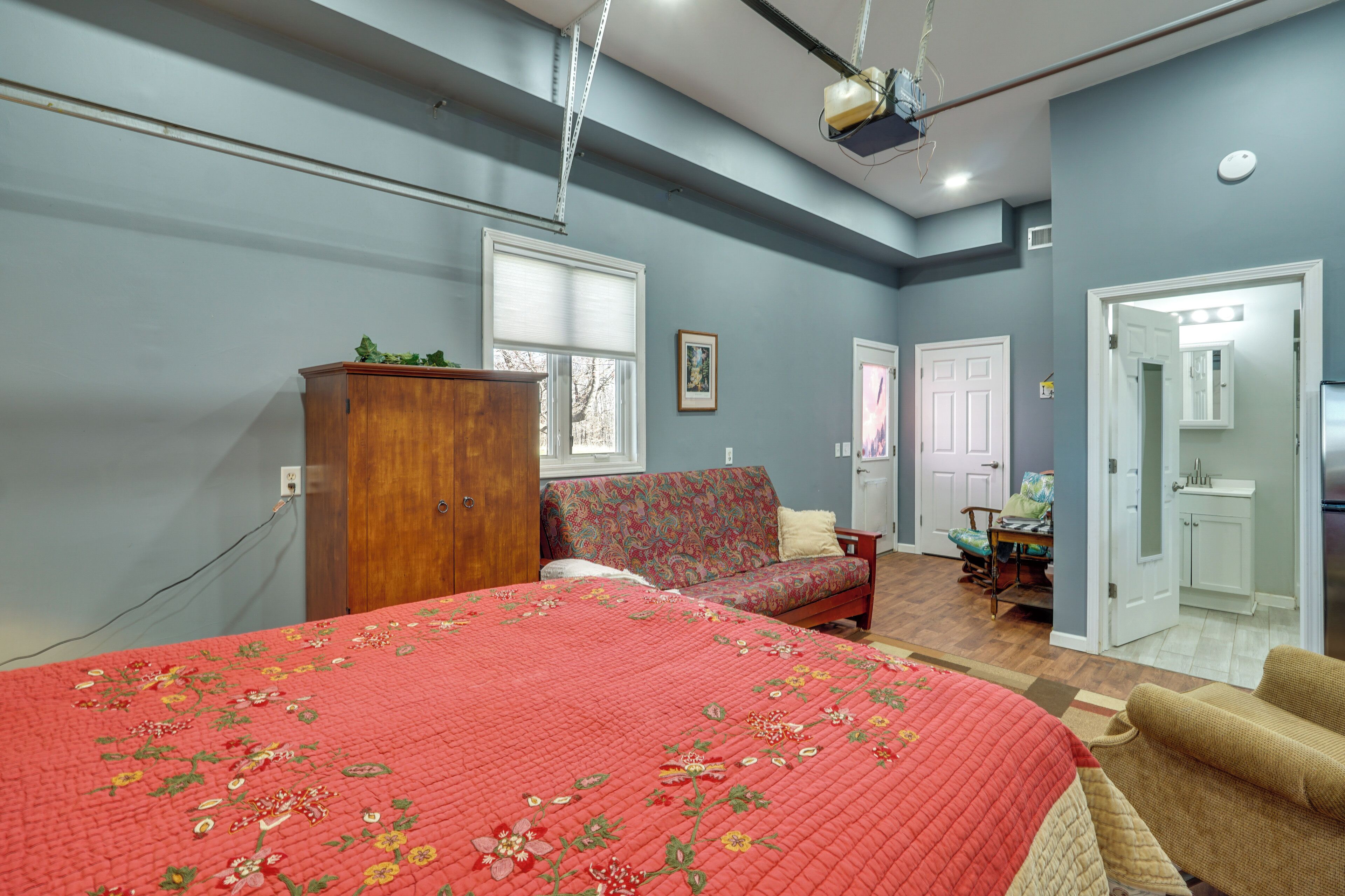 A bedroom with a bed, a sofa, a wooden cabinet, a desk, and a bathroom.