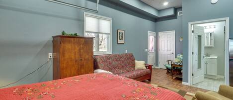 A bedroom with a bed, a sofa, a wooden cabinet, a desk, and a bathroom.