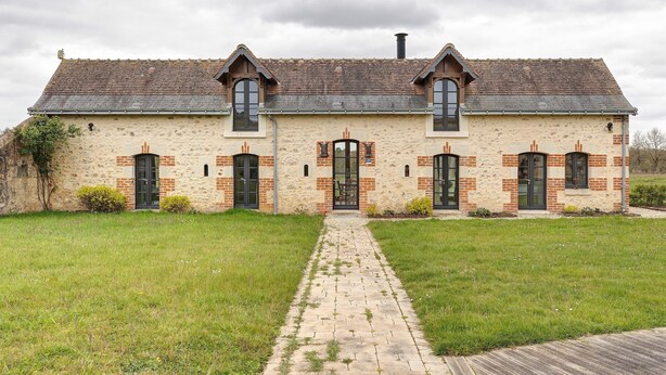 A stone building with a tiled roof, a central entrance, and a brick facade.