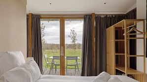 A bedroom with a large bed, a wooden wardrobe, and a view of a grassy field through a glass door.