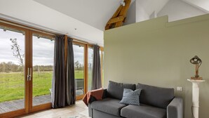 A living room with a grey sofa, a white pedestal table, and a view through large glass doors to an outdoor area.