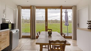 A kitchen with a dining area, a view of the outdoors, and a large window with curtains.