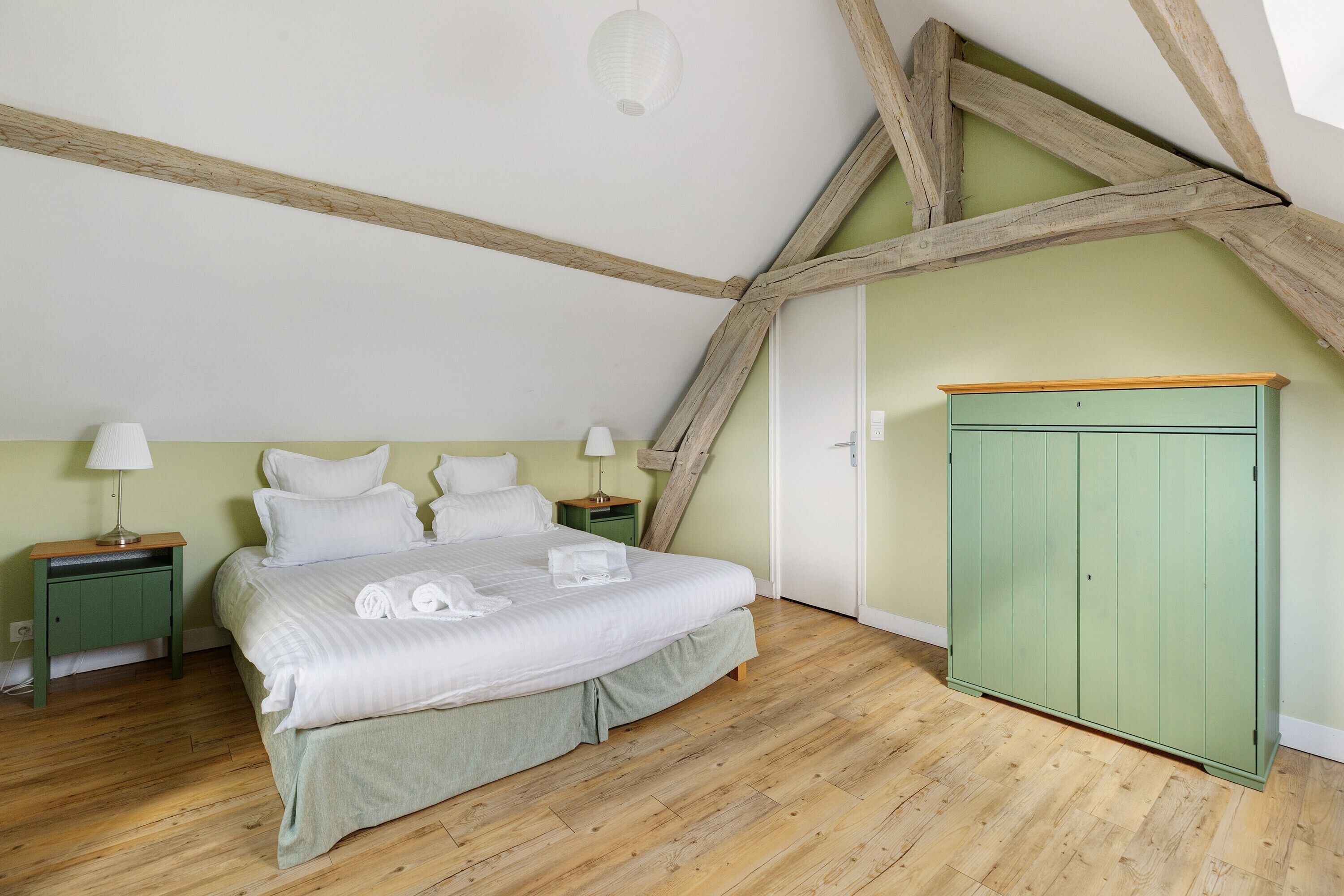 A bedroom with a bed, nightstands, a wardrobe, and exposed wooden beams.