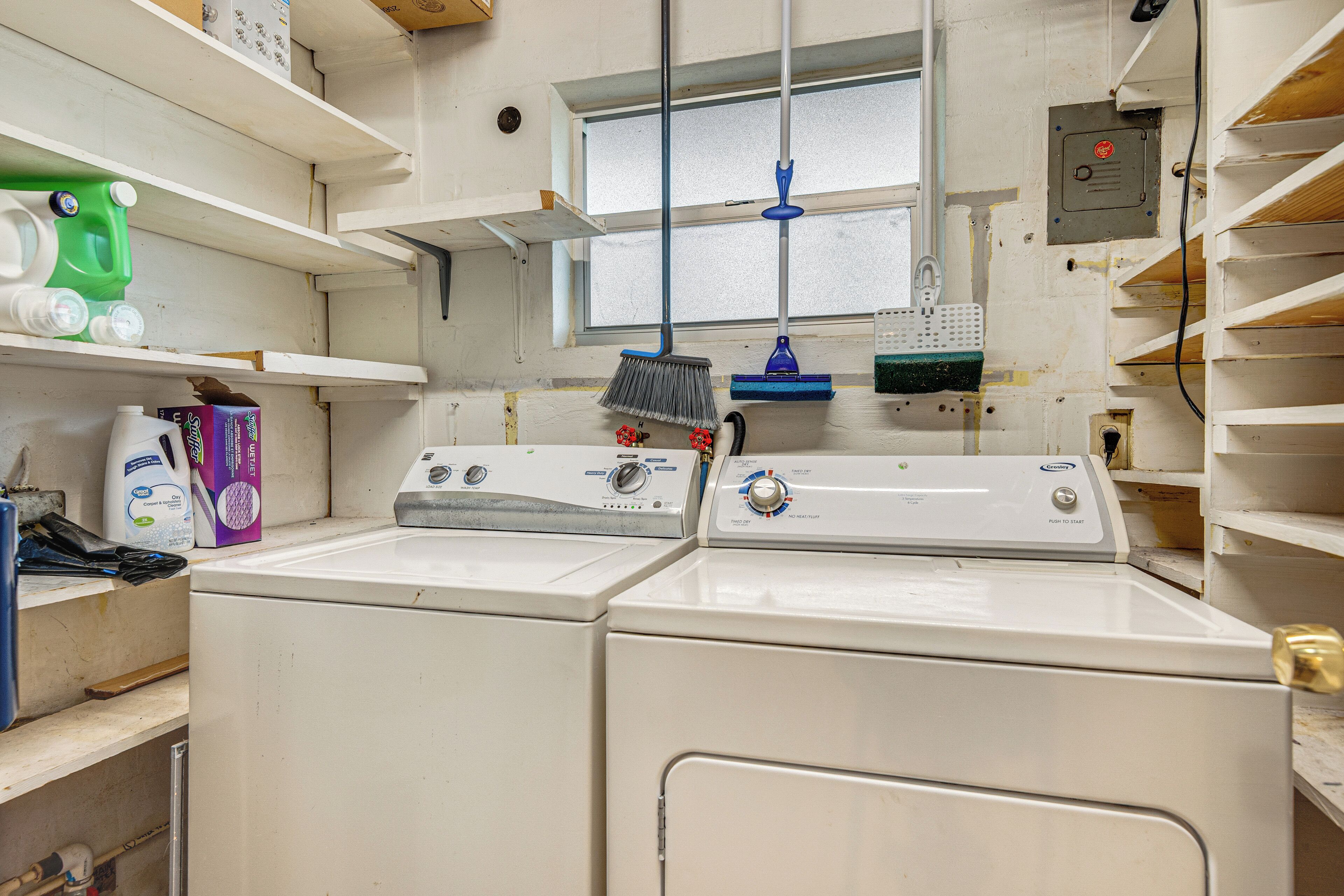 A laundry room with two stacked washers and dryers, shelves with cleaning supplies, and a window with a view.