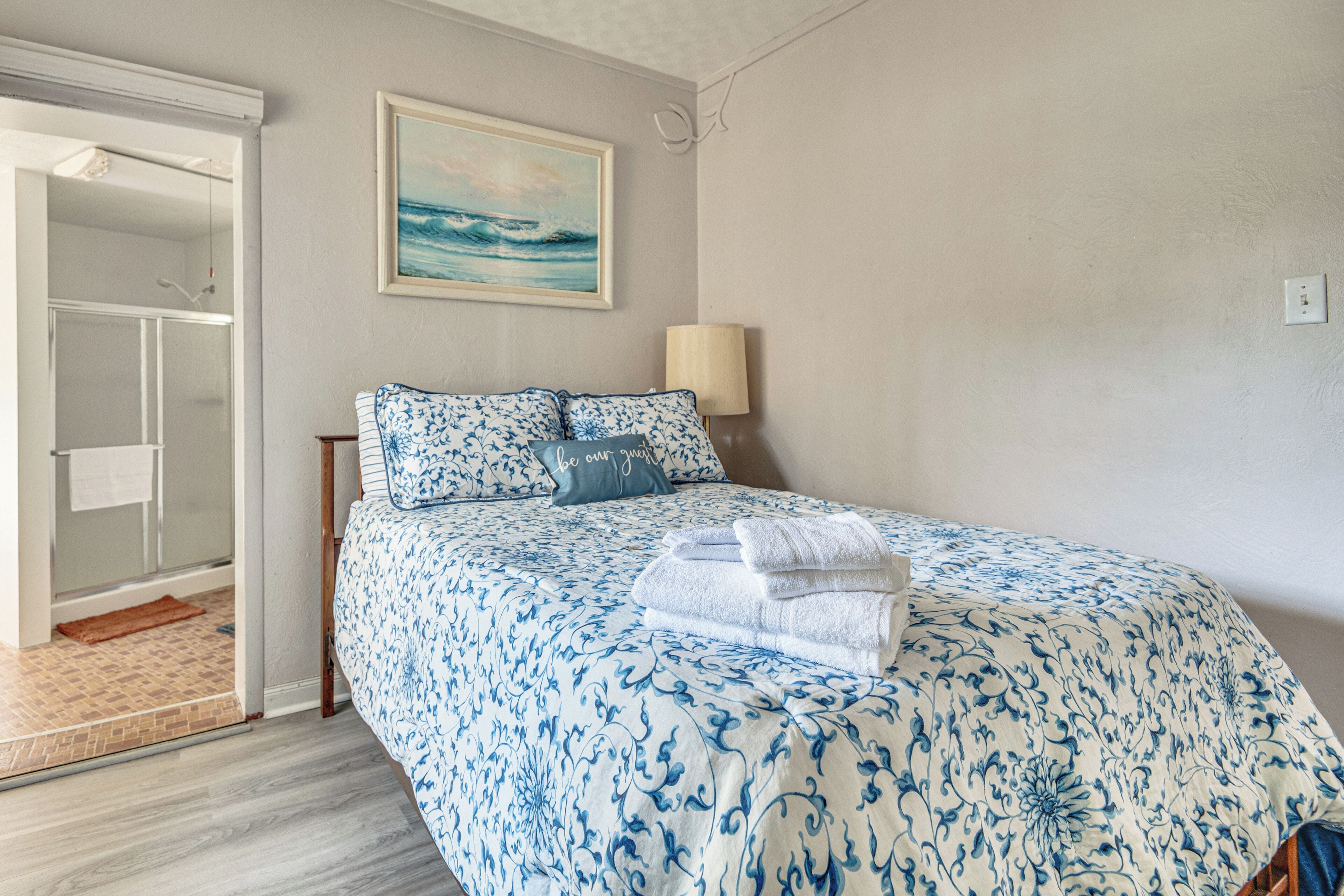 A bedroom with a bed, a painting, a nightstand, and a lamp.