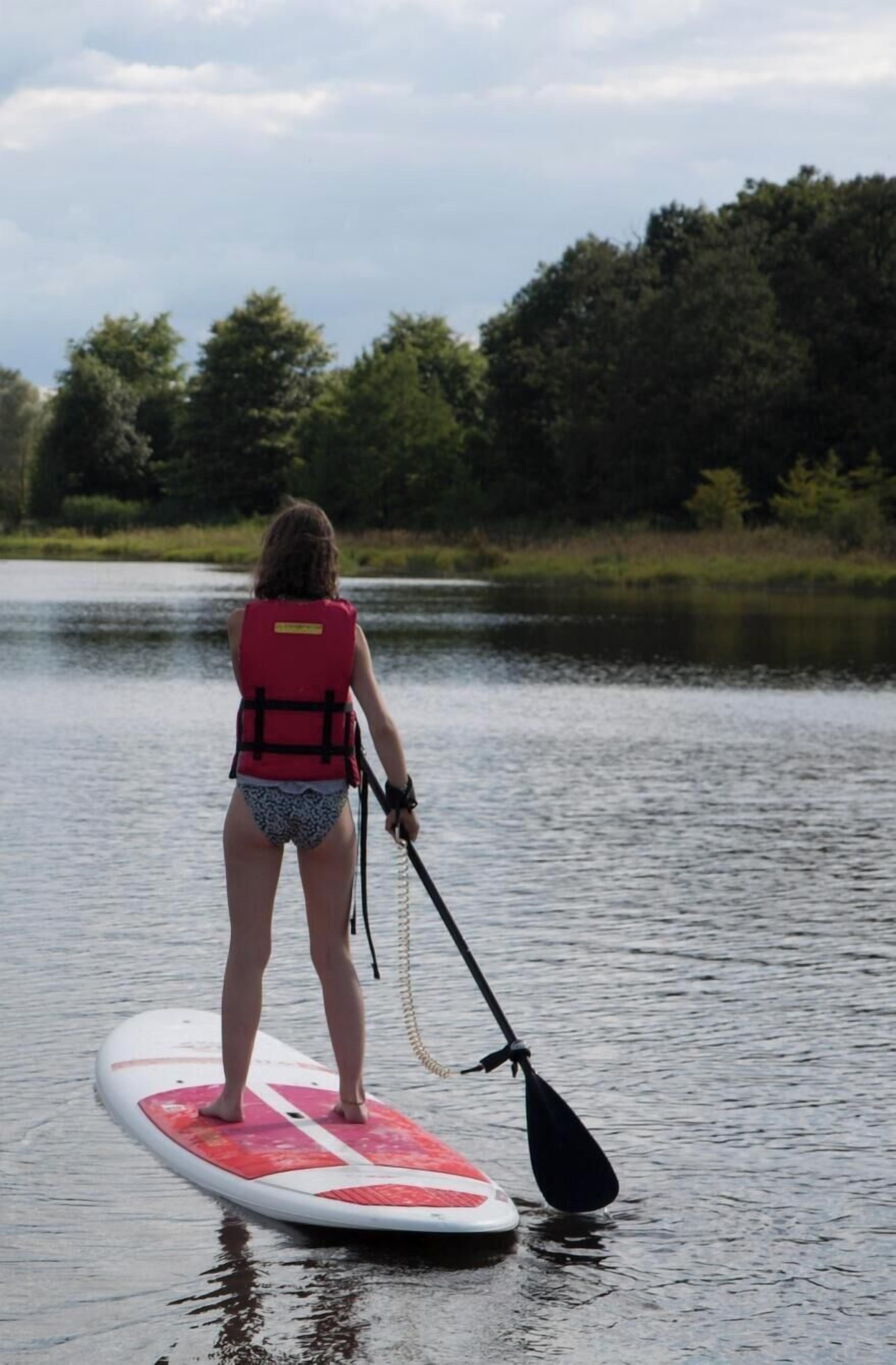 Uma pessoa praticando paddleboard em um lago calmo, com árvores ao fundo.