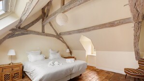 A bedroom with a sloped ceiling, a bed with white linens, a nightstand with a lamp, and a chair.