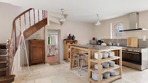 A kitchen with a wooden staircase, a central island with stools, and a built-in oven.