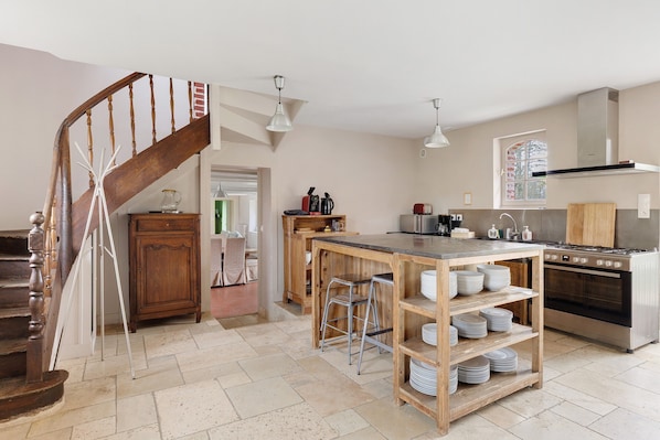Une cuisine avec un escalier en bois, un îlot central doté de tabourets et un four encastré.