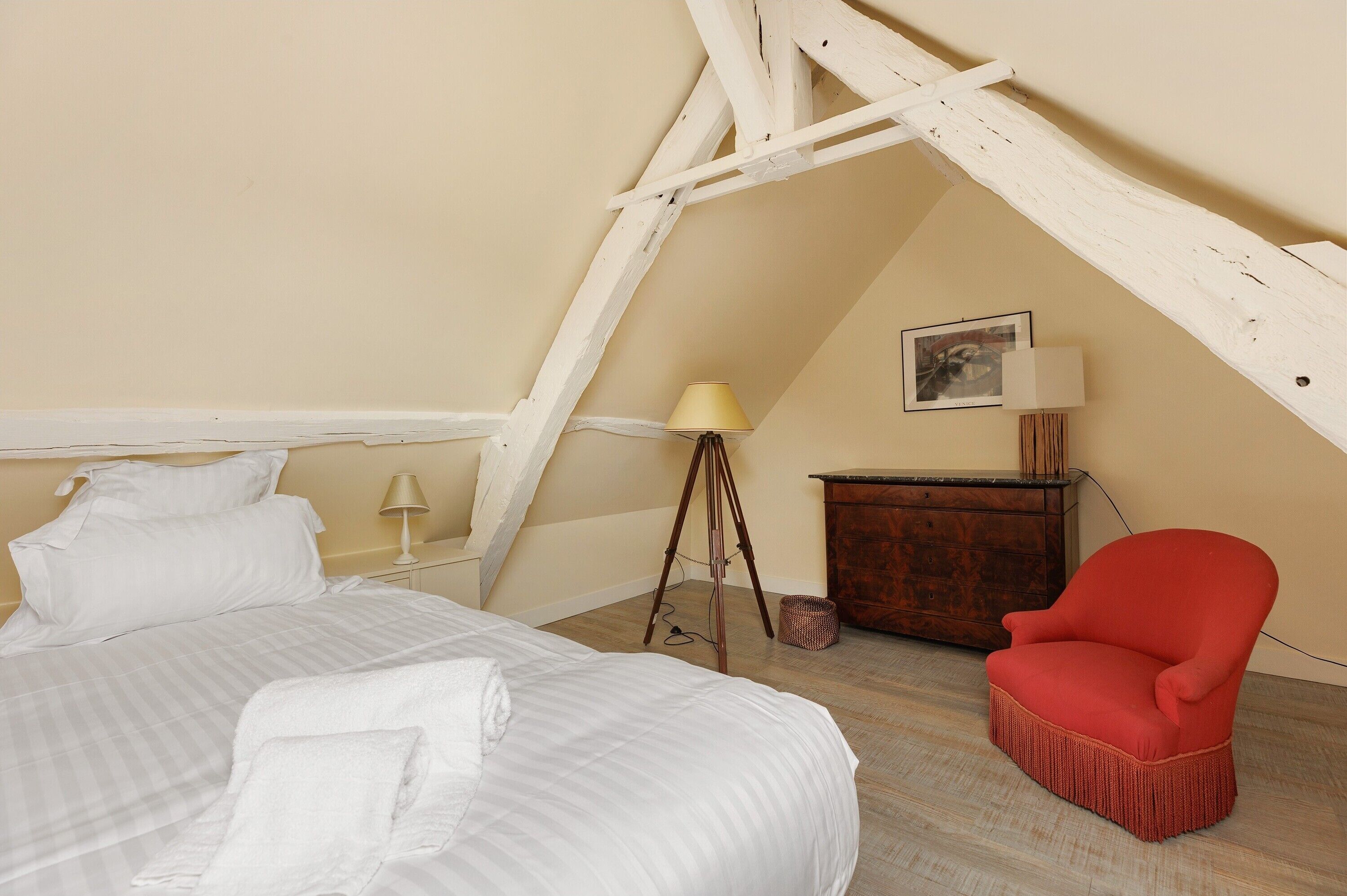 A bedroom with a bed, a red chair, a wooden dresser, and a lamp.