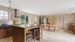 A kitchen with a central island, bar stools, a dining table with chairs, and a refrigerator.