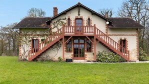 Una casa a due piani con una scala in legno che conduce a un balcone, immersa in un prato.