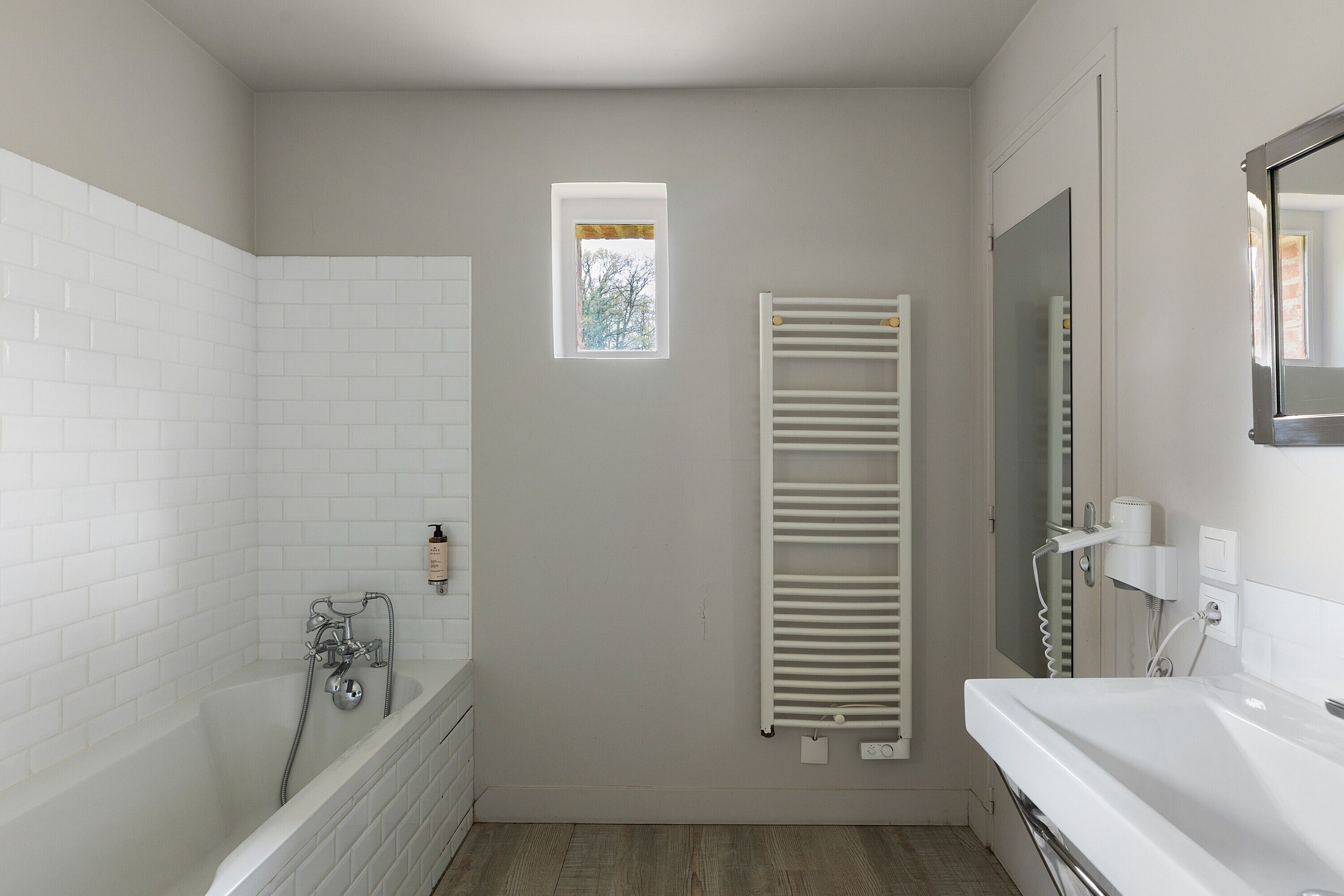 Une salle de bain avec une baignoire, une douche, une petite fenêtre, un porte-serviettes et un miroir.