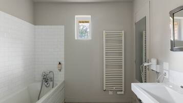 Une salle de bain avec une baignoire, une douche, une petite fenêtre, un porte-serviettes et un miroir.