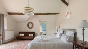 Una camera da letto con un letto grande, una testiera in legno, un comodino con una lampada, uno specchio rotondo a parete e un tappeto decorato sul pavimento.