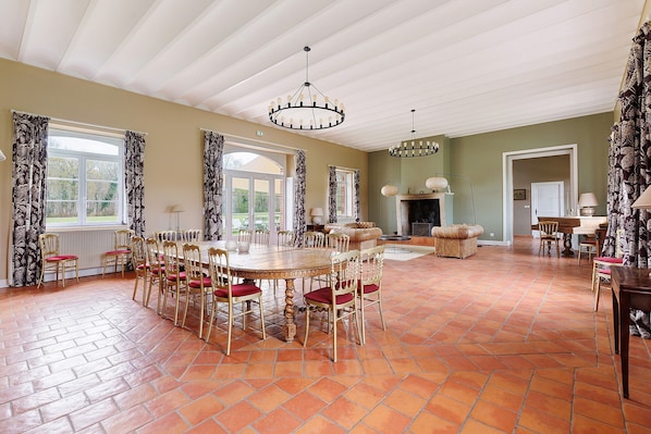 A spacious dining room with a large wooden table and chairs, a fireplace, and a view of the outdoors through large windows.