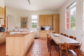 A kitchen with a central island, wooden cabinets, a dining table with chairs, and a large window.