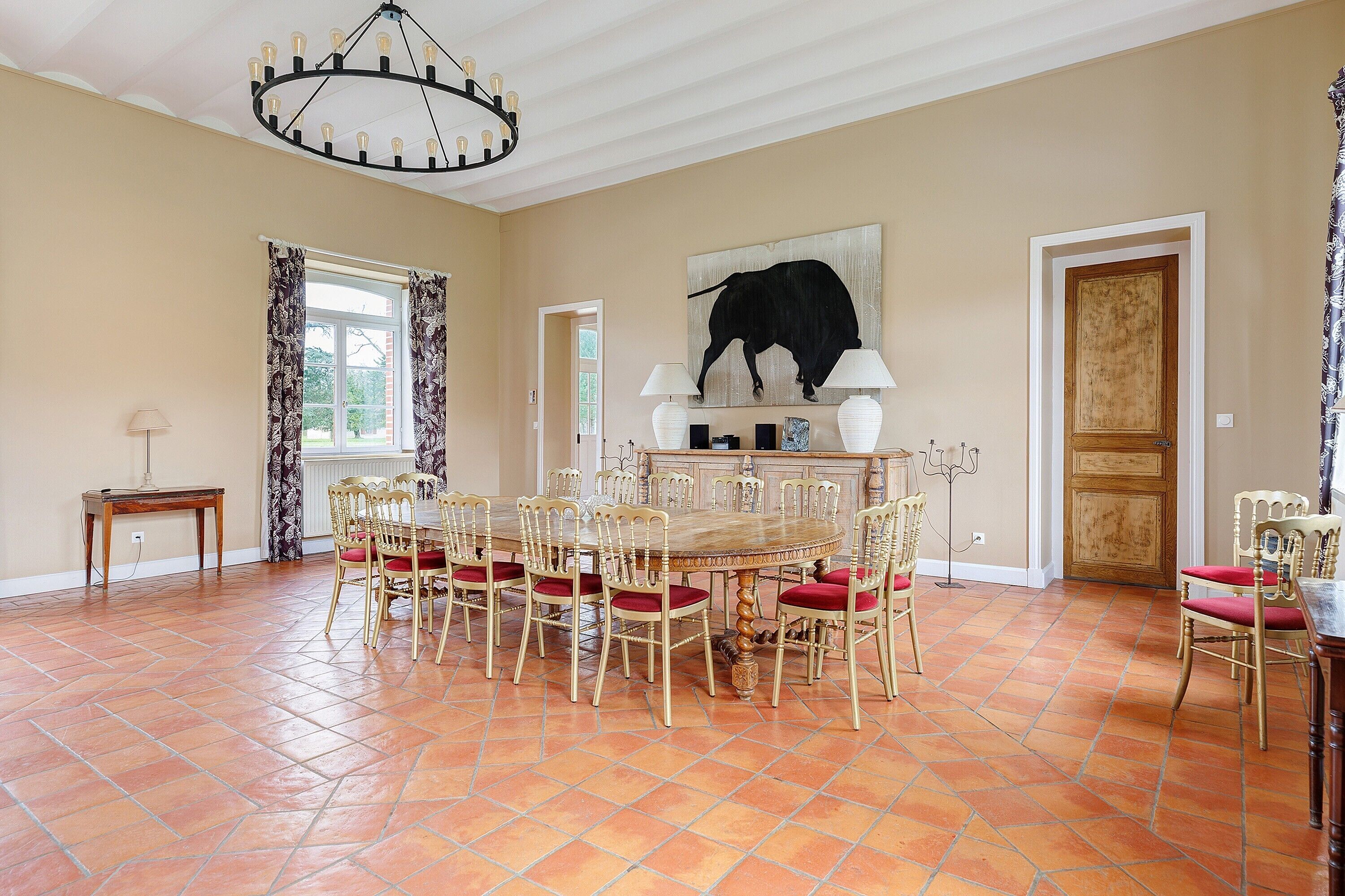 Un coin repas avec une table ronde, des chaises, un lustre et un tableau représentant un taureau accroché au mur.