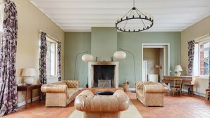 Ein Wohnzimmer mit Kamin, zwei Sofas, einem Klavier und einer Kristallleuchter.