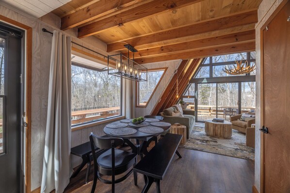A modern interior with a wooden ceiling, large windows, a dining area with round tables, and a cozy seating area.