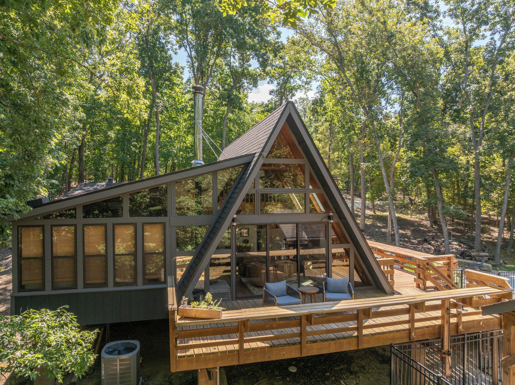 A modern cabin with a sloped roof, large windows, and a deck with outdoor seating.